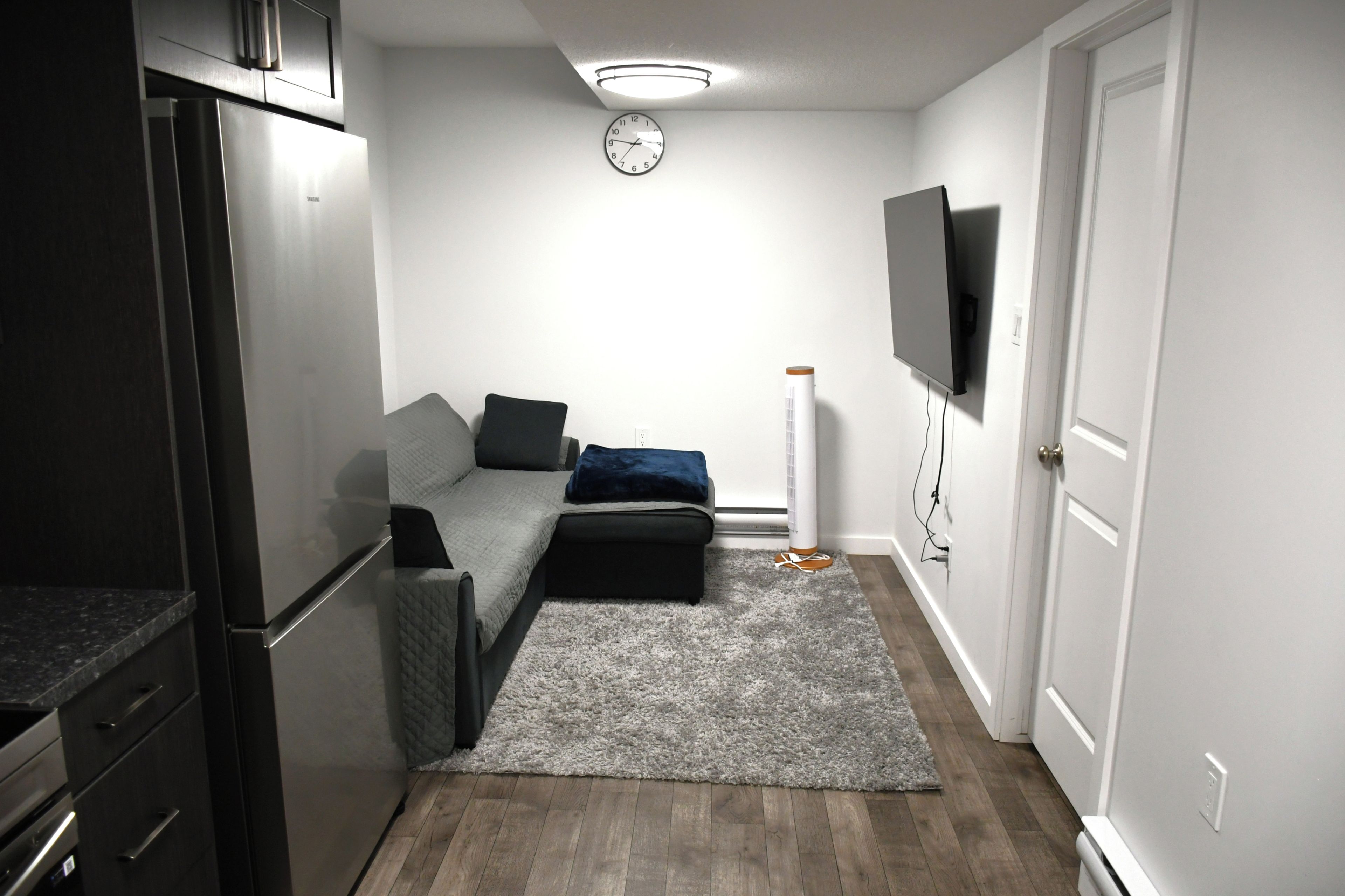 A compact living space with a kitchenette, a sofa, a TV, and a clock on the wall.