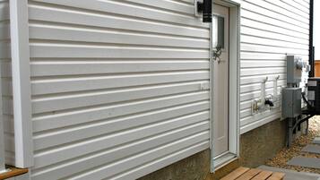 A modern exterior with a white siding wall, a metal door, and a concrete pathway leading to a wooden bench.