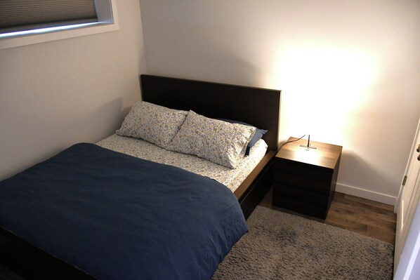 A bedroom with a bed, a nightstand, a lamp, and a window.