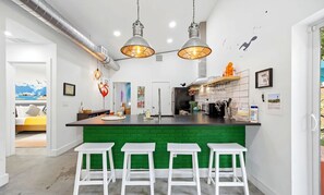 A modern kitchen with a green island, white bar stools, pendant lighting, and a view into the adjacent living area. - Unique wedge house 1.5 miles from historic district. Amazing for families! (St. Augustine)