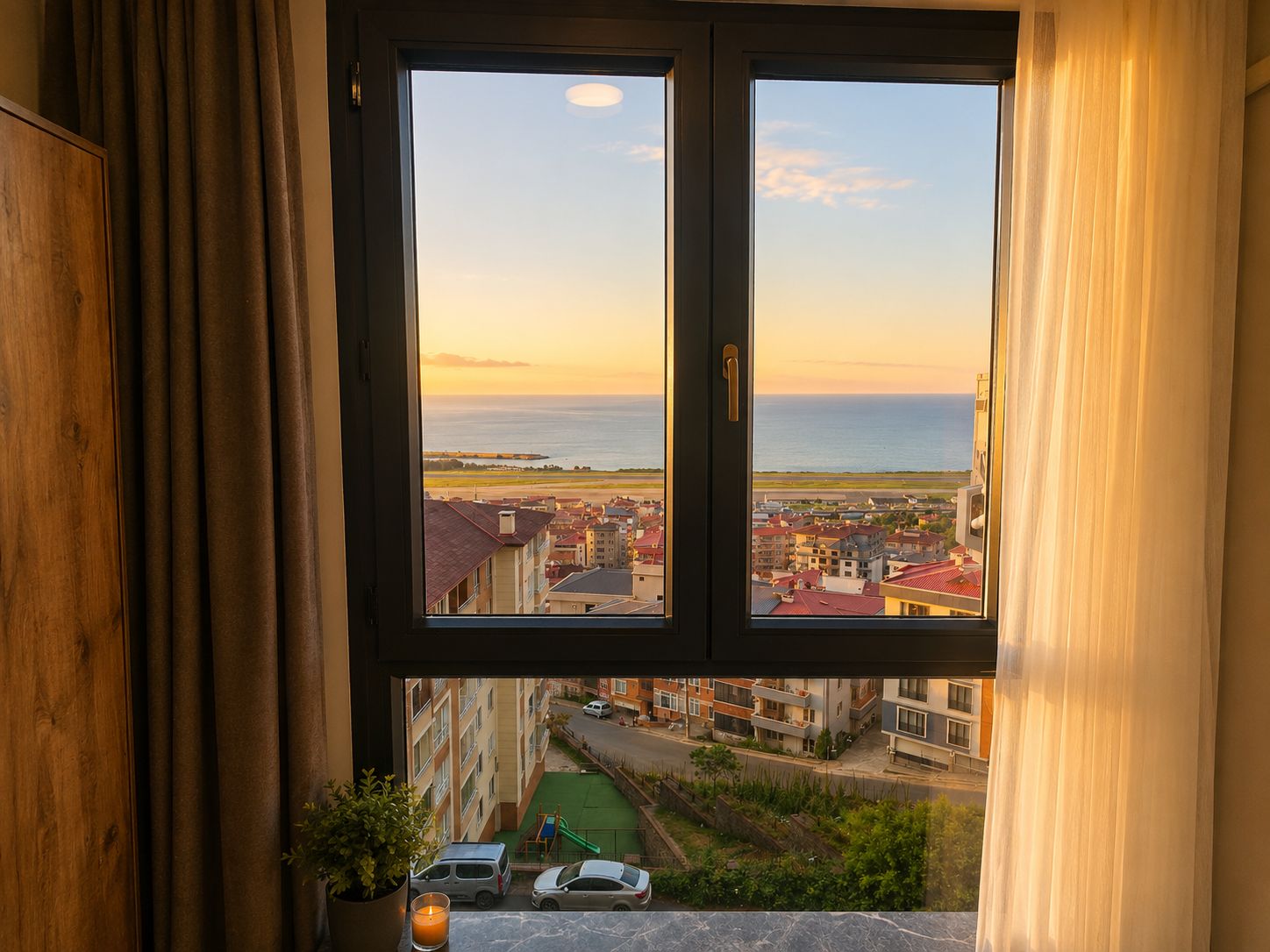 Una ventana con vistas a un pueblo costero y una playa al atardecer.