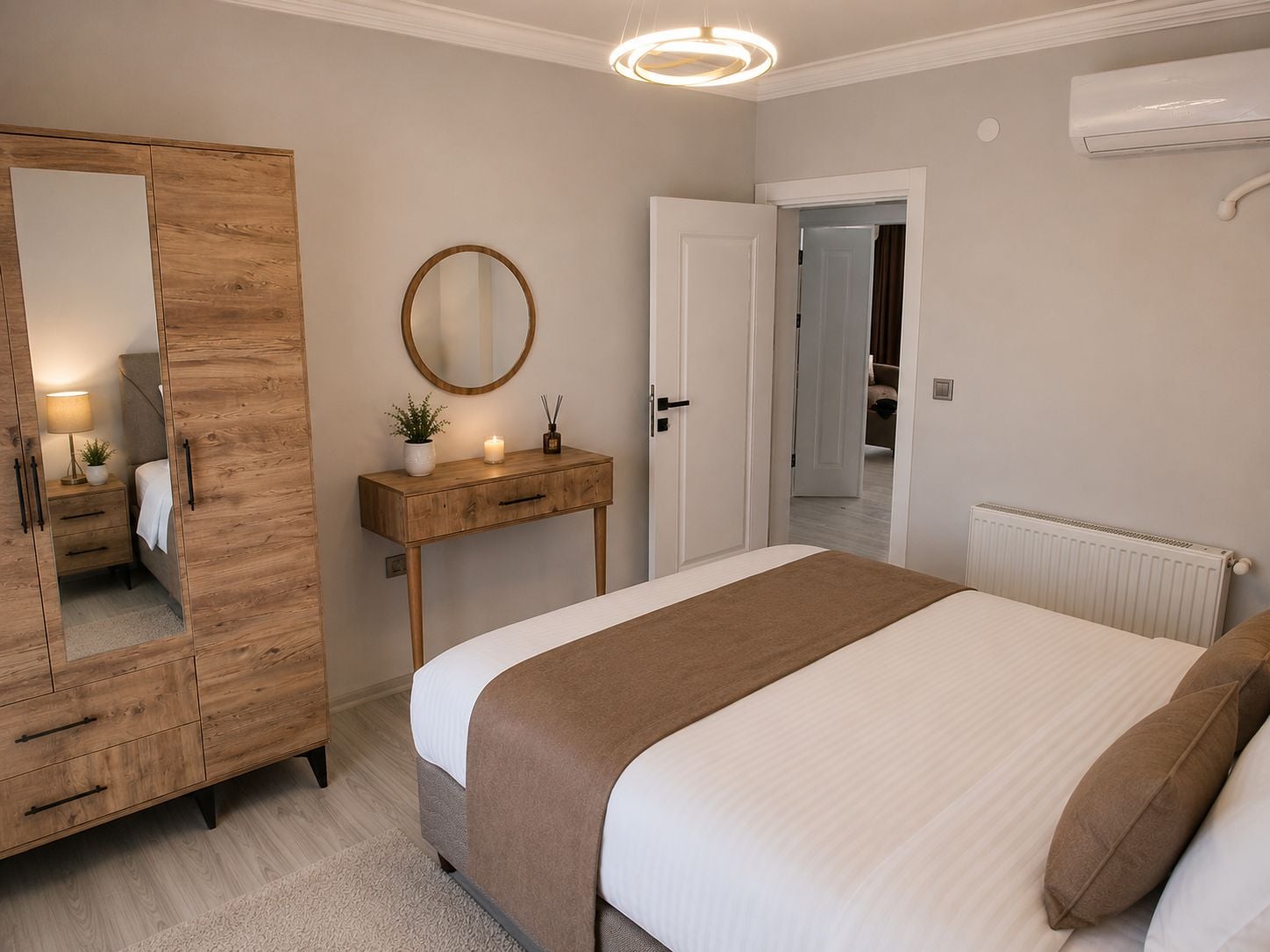 Una camera da letto con un letto, un armadio in legno, un comodino con una lampada, uno specchio e una porta che dà su un'altra stanza.