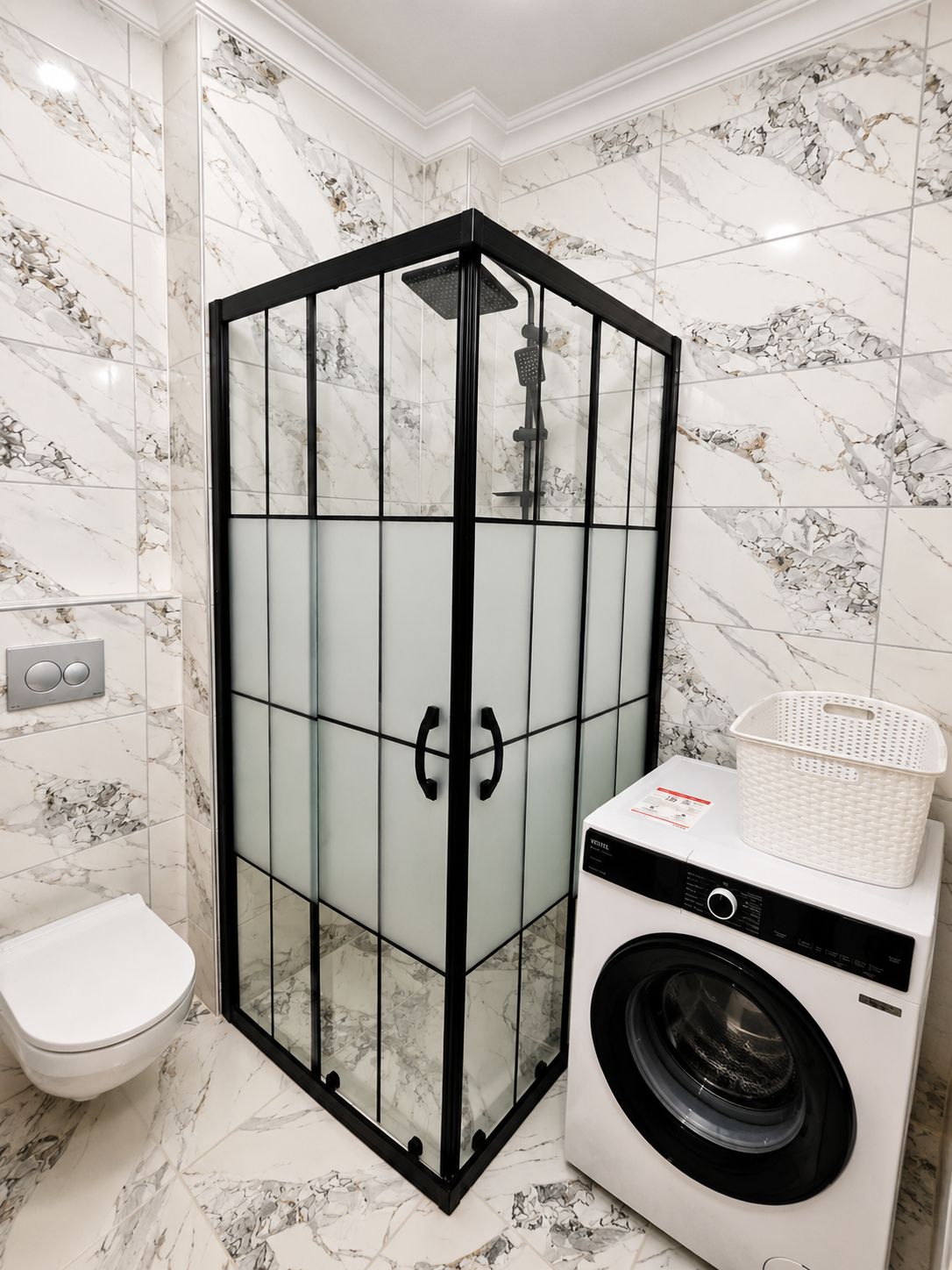 A bathroom with a glass-enclosed shower, a washing machine, and a toilet.