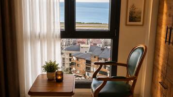 Una stanza con vista mare, una sedia di legno, un tavolino con una pianta e un armadio.