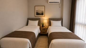 A hotel room with two beds, a nightstand with a lamp, a framed picture on the wall, and an air conditioning unit.