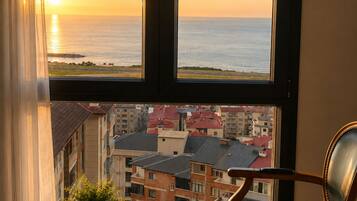 A room with a large window overlooking a cityscape and the sea at sunset.