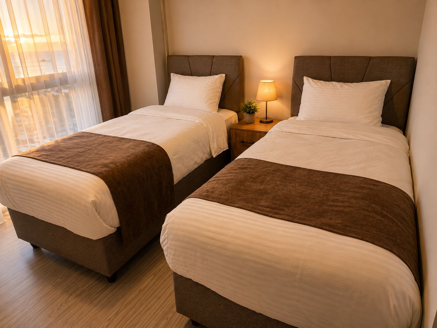 Una habitación de hotel con dos camas, una mesita de noche con lámpara y un ventanal con cortinas.