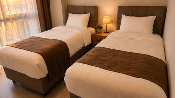 Una habitación de hotel con dos camas, una mesita de noche con lámpara y un ventanal con cortinas.