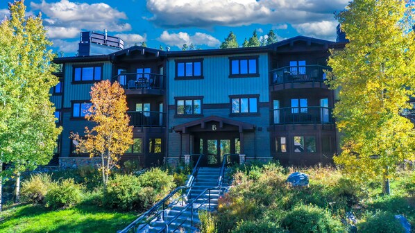 A multi-story building with a central entrance, surrounded by lush greenery and trees. - Walk to Lifts & Main St | Hot Tub (Breckenridge)