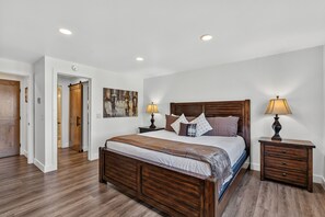 Une chambre à coucher avec un lit en bois, deux tables de chevet, une commode, une porte et un tableau au mur.
