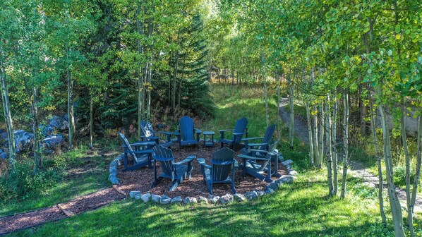 An outdoor seating area with Adirondack chairs arranged around a fire pit, surrounded by a stone border. - Walk to Lifts & Main St | Hot Tub (Breckenridge)