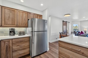 Eine moderne Küche mit Holzausstattung, einem Edelstahlkühlschrank, einem eingebauten Toaster und einem Essbereich mit Tisch und Stühlen.