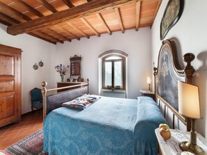 Ein Schlafzimmer mit einem Bett, Holzbalkendecke, einem Schminktisch, einem Spiegel und einem Fenster.