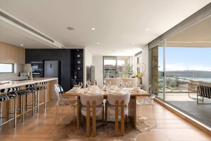 A modern kitchen with a dining area, large windows, and a view of the sea. - Mosman Penthouse | Harbour Views + Parking (Mosman)
