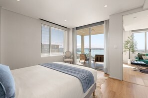Une chambre moderne avec un grand lit, un balcon aménagé avec des sièges et une vue sur la mer.