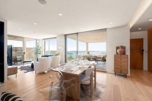 Un vaste espace de vie comprenant un coin repas avec une table pour quatre personnes, un canapé et une vue sur la mer.