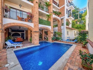 A multi-level residential building with a swimming pool, outdoor seating, and balconies with plants. - Cozy Mexican-style oceanfront apartment located 5 minutes away from Puerto Vallarta's main area. (Puerto Vallarta)