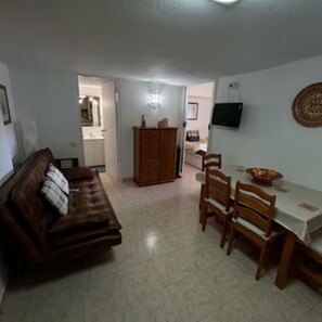 A living room with a brown leather sofa, a wooden dining table with chairs, and a kitchen in the background. - Apartment near Falésia Beach (Albufeira)