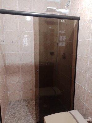Une cabine de douche fermée par des parois en verre, avec un cadre noir, des carreaux de couleur beige et une pomme de douche visible.