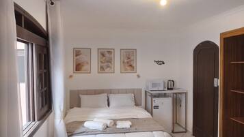 Une chambre à coucher avec un lit, une table de chevet sur laquelle se trouve un micro-ondes, et une porte.