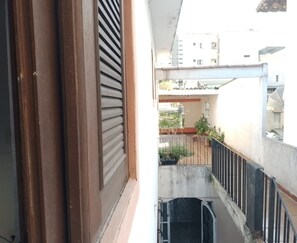 Un balcon avec une balustrade en métal, un pot de fleurs et une vue sur un bâtiment en arrière-plan.