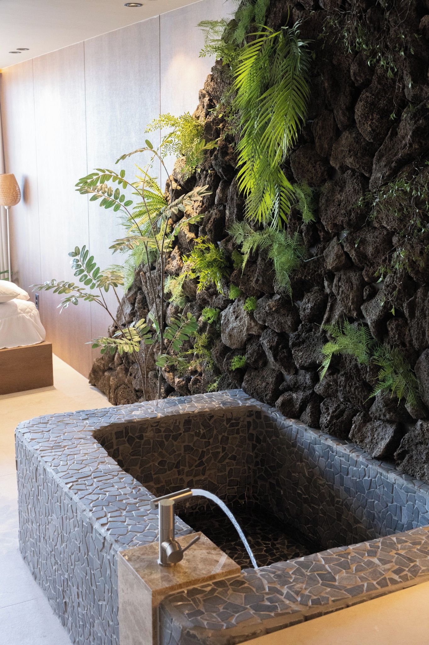 A spa area with a stone tub, a wooden wall with greenery, and a white floor.
