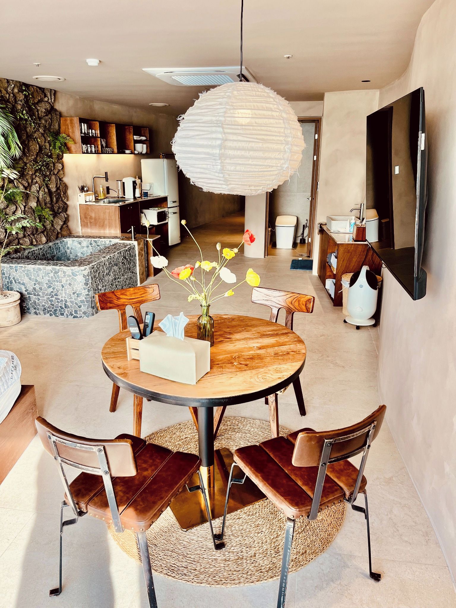A modern living room with a round wooden table, leather chairs, and a hanging light fixture.