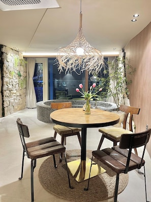 A round dining table with four chairs, a hanging light fixture, and a vase with flowers. - Lumiere (Busan)