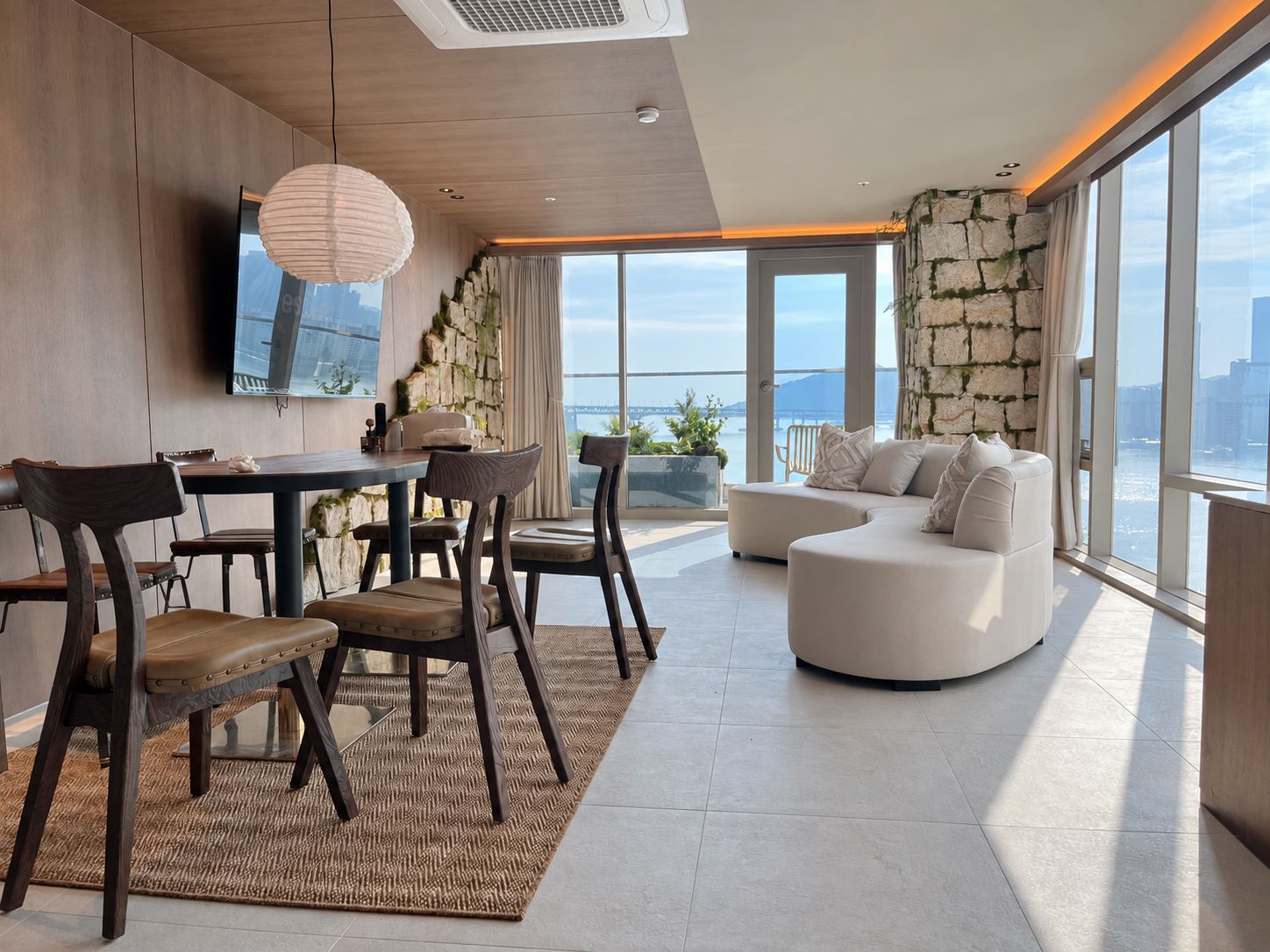 A modern living room with a dining area, large windows, and a stone accent wall.