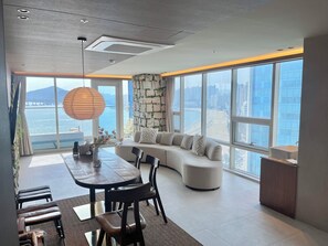 A modern interior with a dining area, seating, and a large window offering a city view. - Lumiere (Busan)