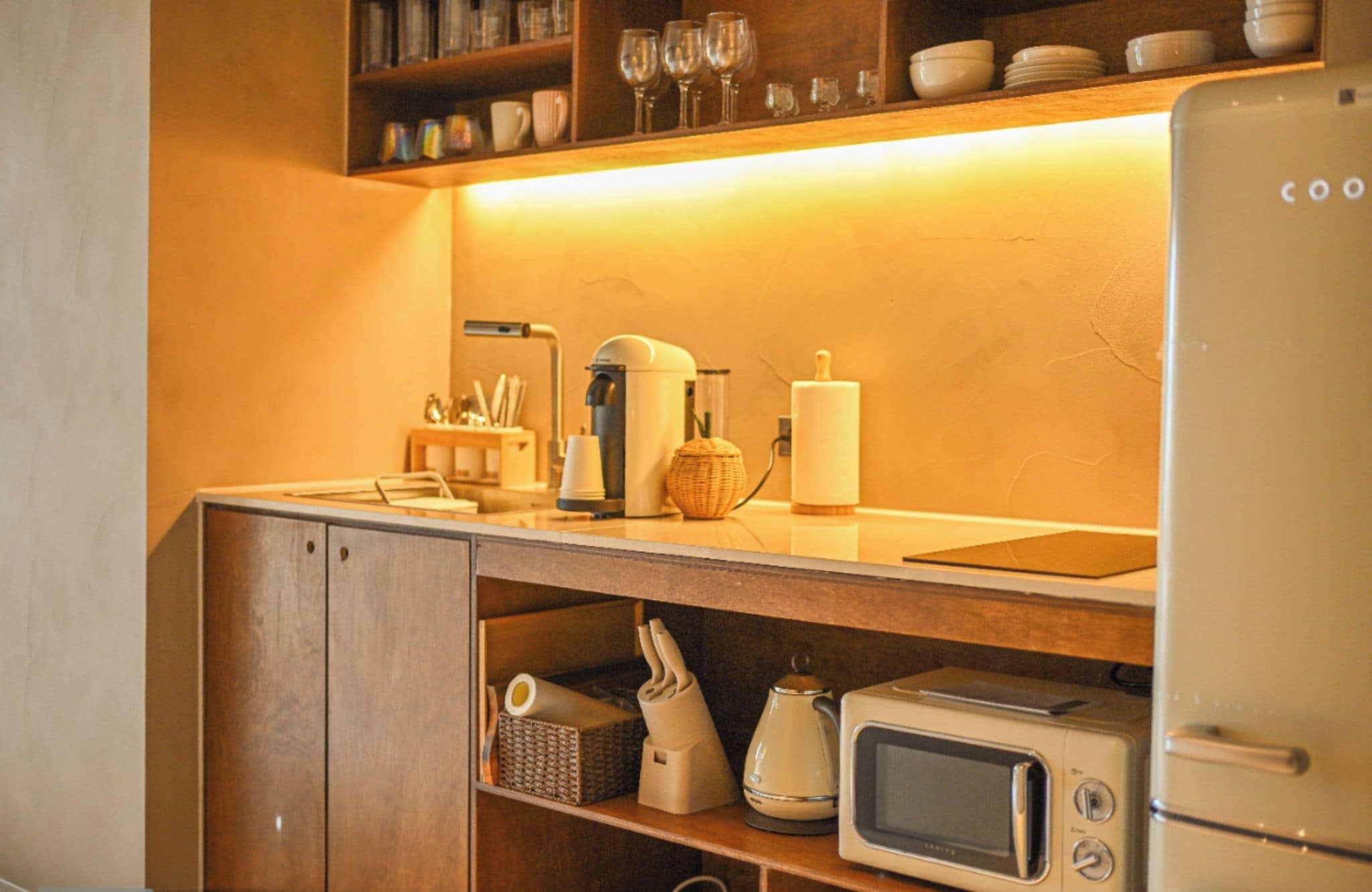Une cuisine équipée d’un four à micro-ondes, d’un grille-pain et d’une machine à café sur le plan de travail, et d’un réfrigérateur sur la droite.