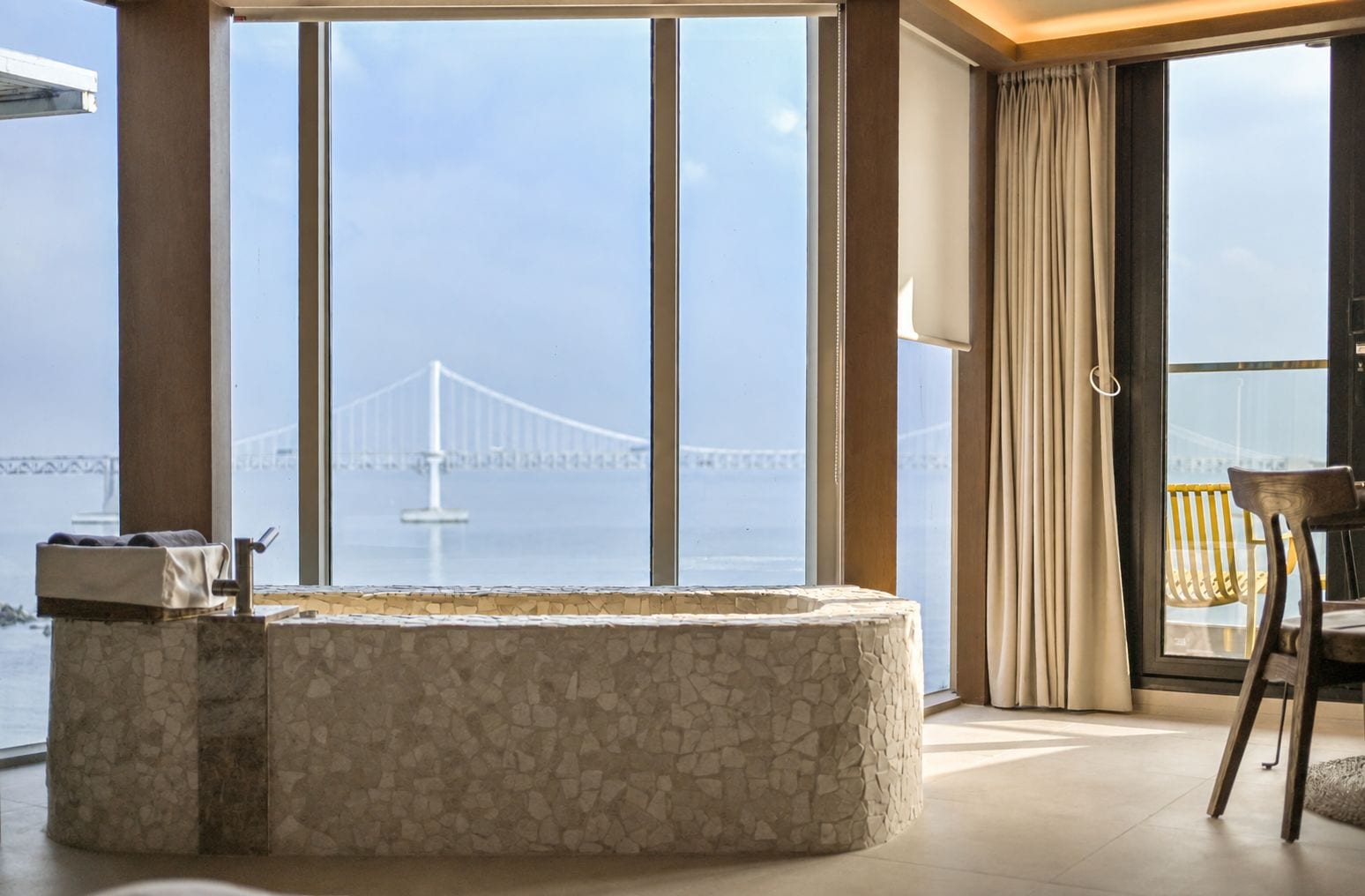 Une salle de bain moderne avec un lavabo en pierre, de grandes fenêtres et une vue sur un pont.