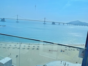 A beach with umbrellas and people, a bridge in the background, and a clear sky. - Lumiere (Busan)