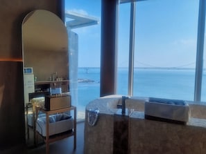 A room with a large window overlooking a bridge and water, a mirror, a bed, and a small kitchenette.