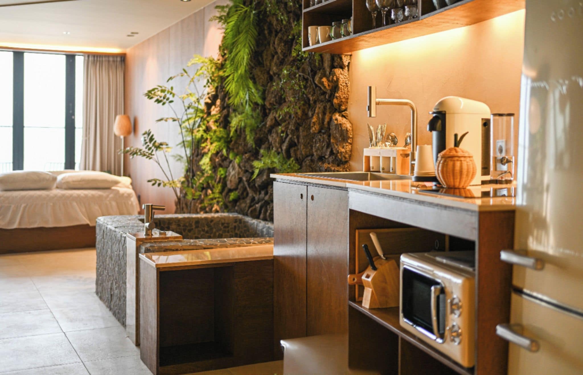 Habitación de hotel moderna con cama, cocina integrada con microondas y un amplio ventanal.