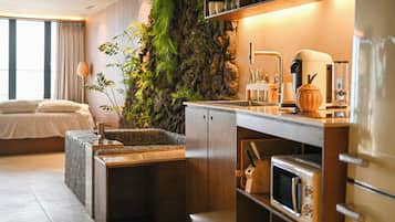 Habitación de hotel moderna con cama, cocina integrada con microondas y un amplio ventanal.