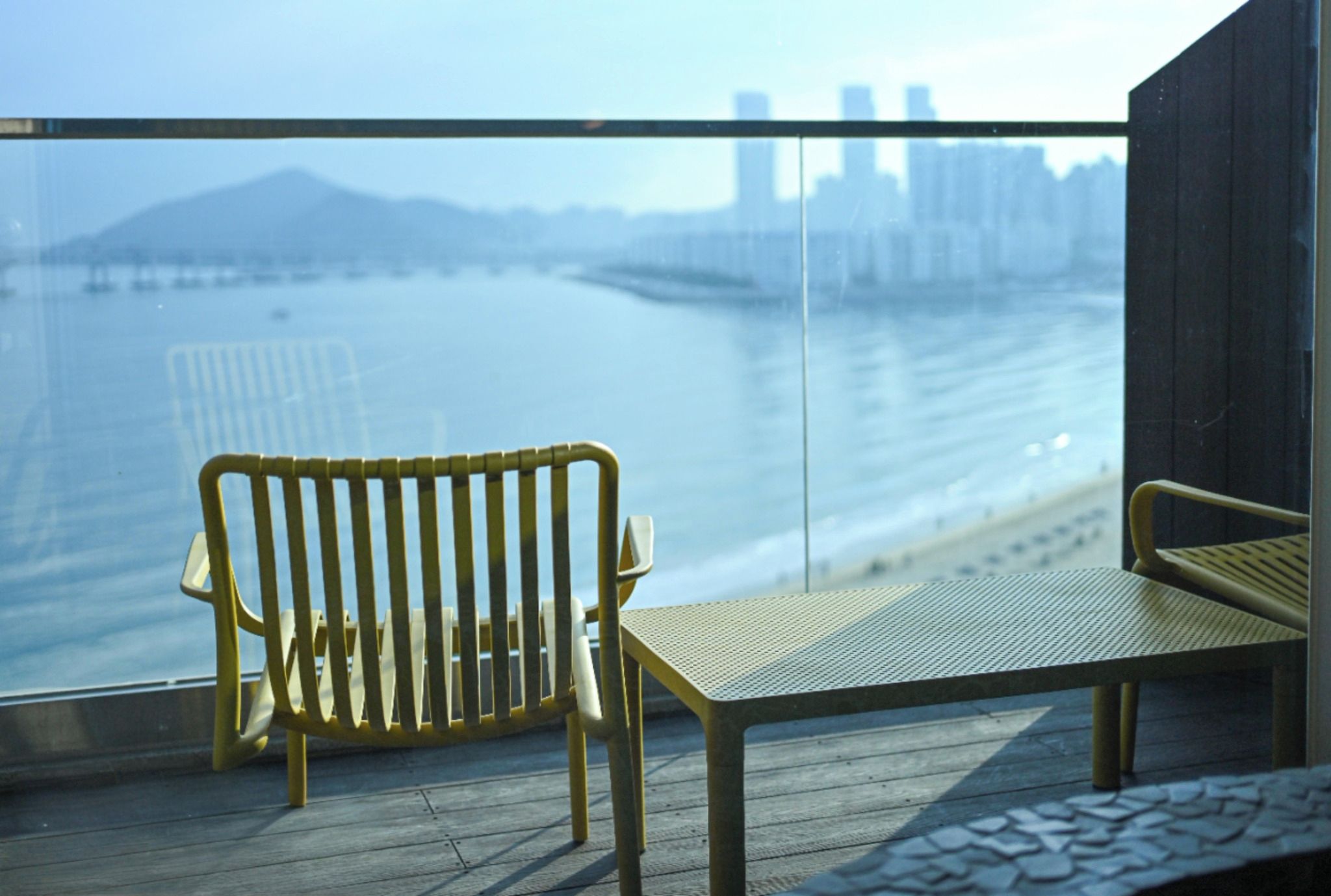A balcony with a bench overlooking a body of water and a distant cityscape.