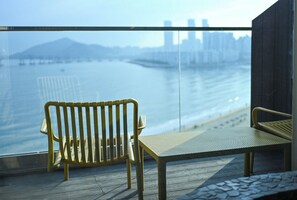 A balcony with a bench overlooking a body of water and a distant cityscape. - Lumiere (Busan)