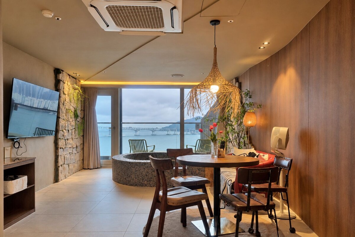 A modern dining area with a round table, chairs, and a view of the water.