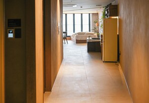 A hotel corridor with a bed, a desk, and a refrigerator. - Lumiere (Busan)