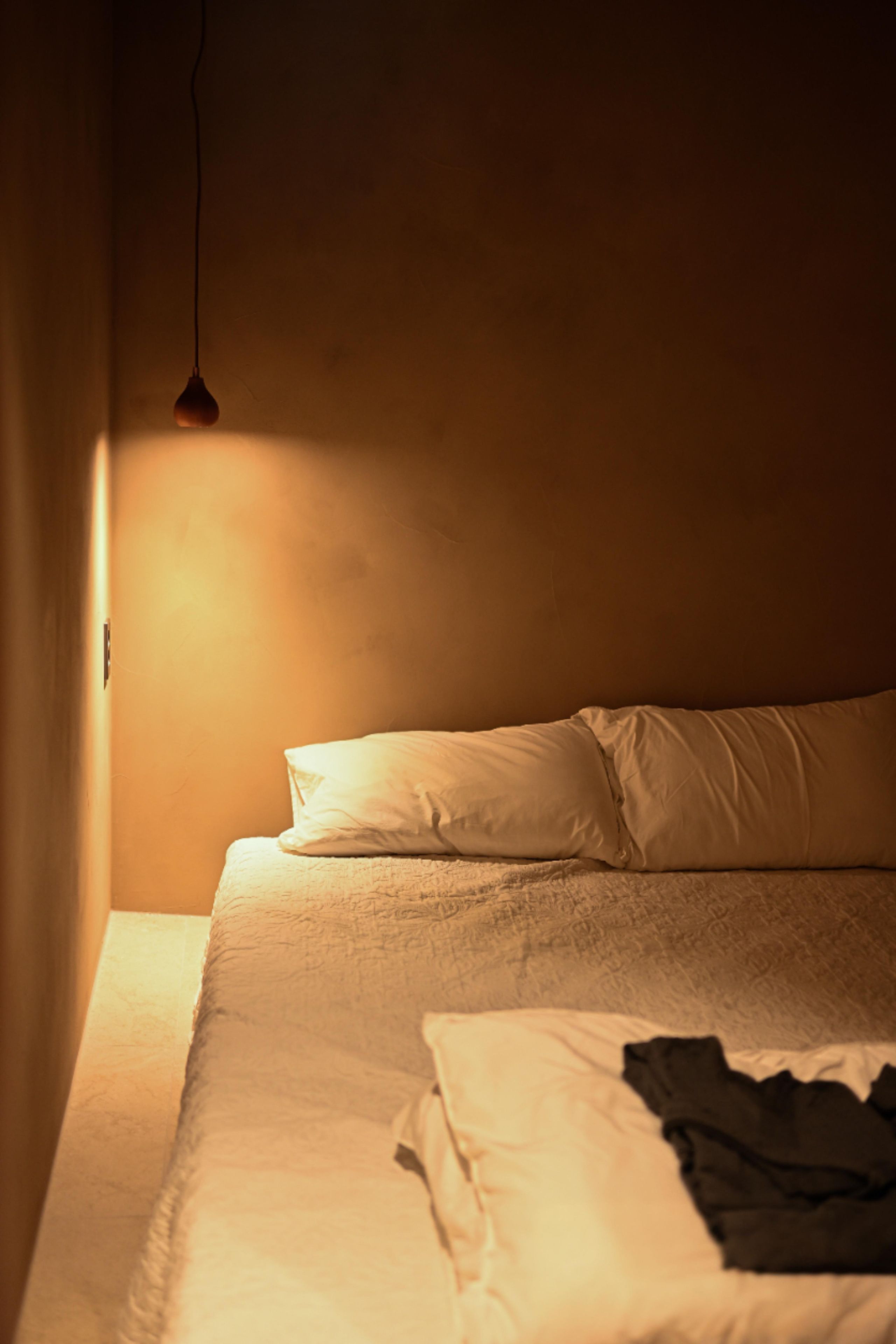 A room with a bed, a hanging light fixture, and a window.