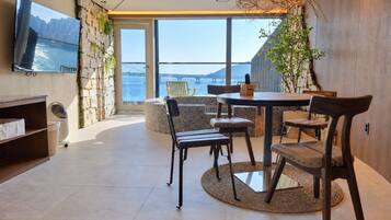 A modern interior with a dining area, a TV mounted on the wall, and a view of the sea through large windows.