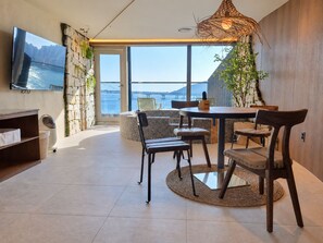 Ein modernes Interieur mit Essbereich, einem an der Wand montierten Fernseher und Meerblick durch große Fenster.