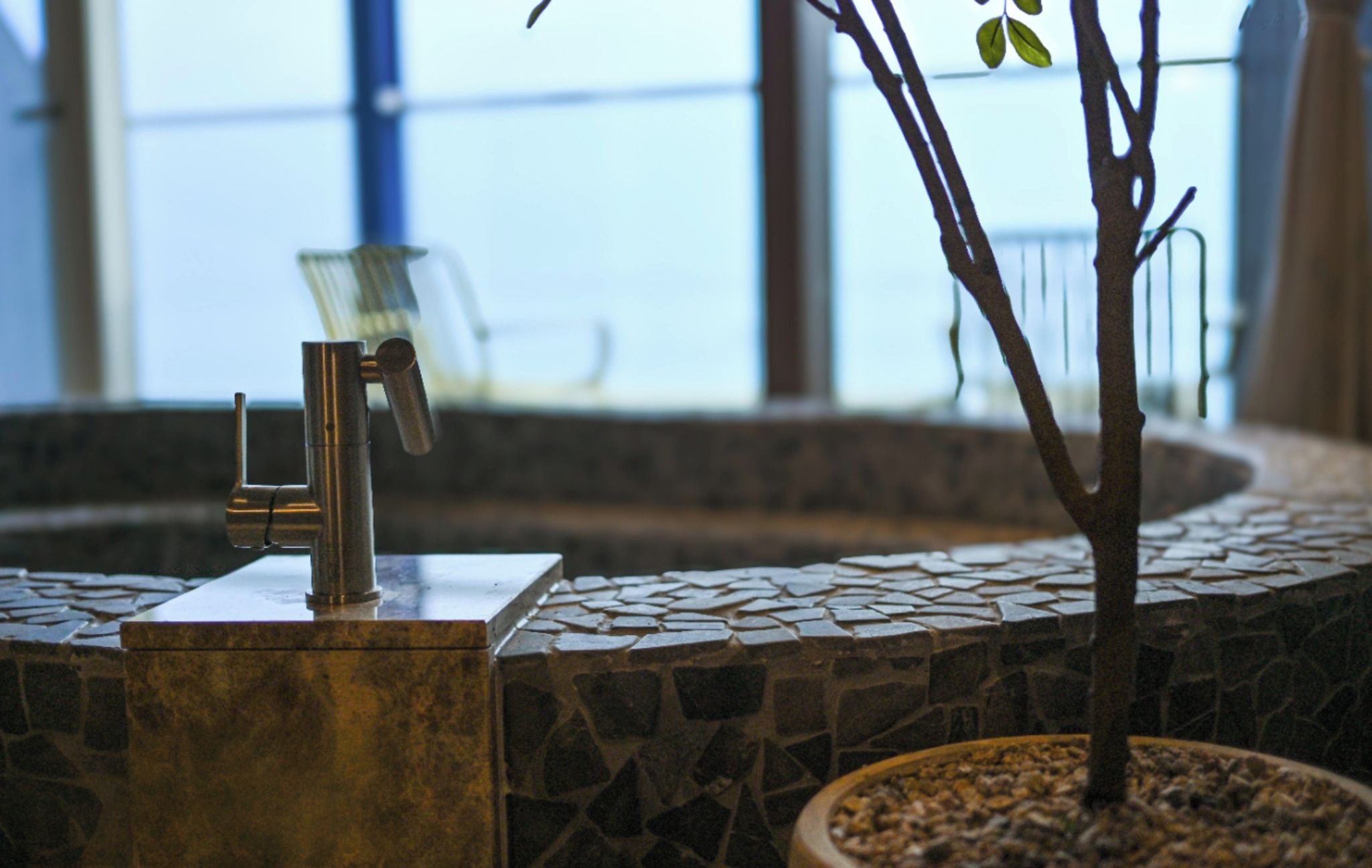 A bathroom with a stone wall, a metal faucet, and a potted plant.