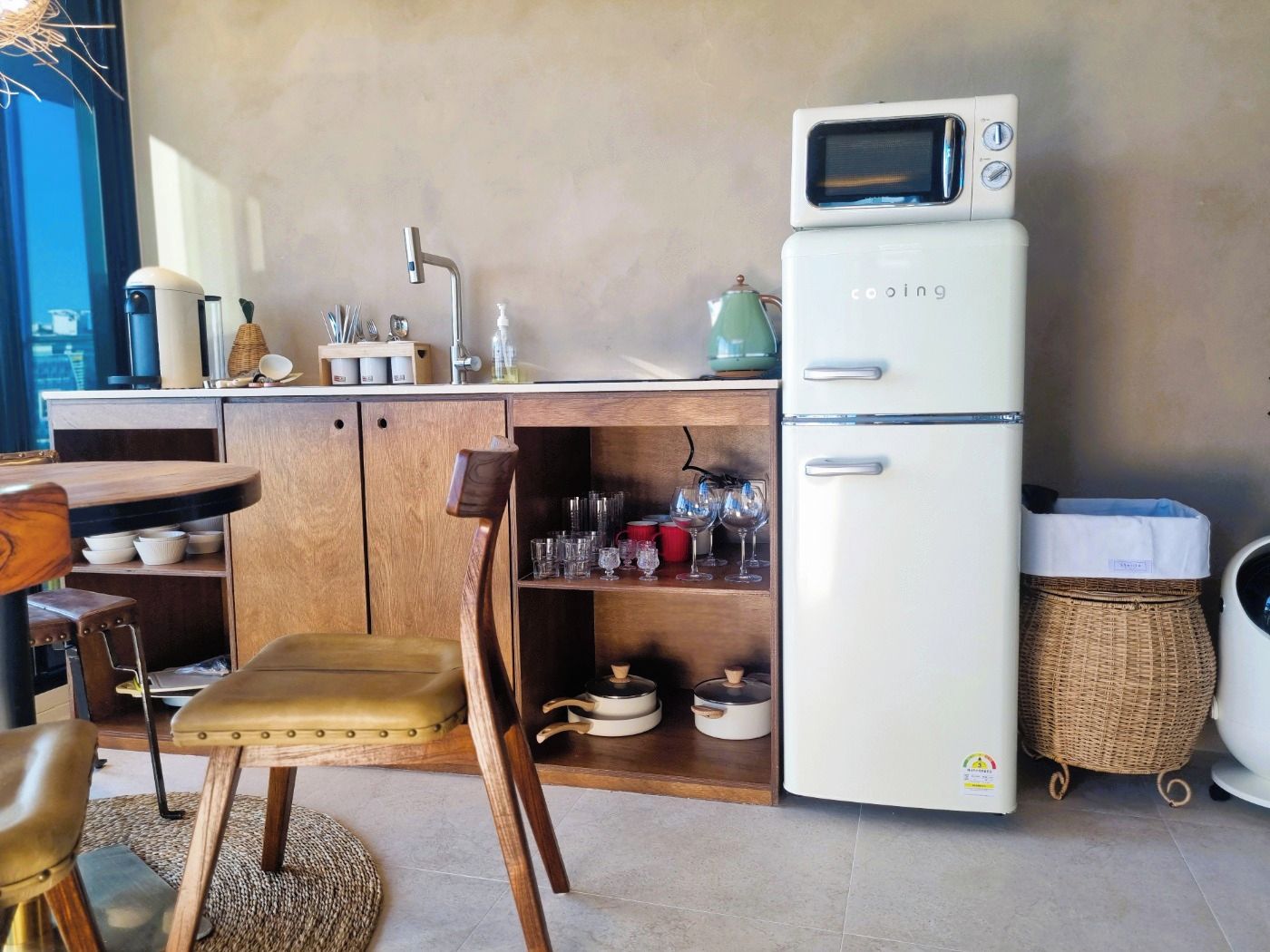 A compact kitchen with a white refrigerator, a sink, and a dining area with a wooden table and chairs.