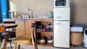 A compact kitchen with a white refrigerator, a sink, and a dining area with a wooden table and chairs.