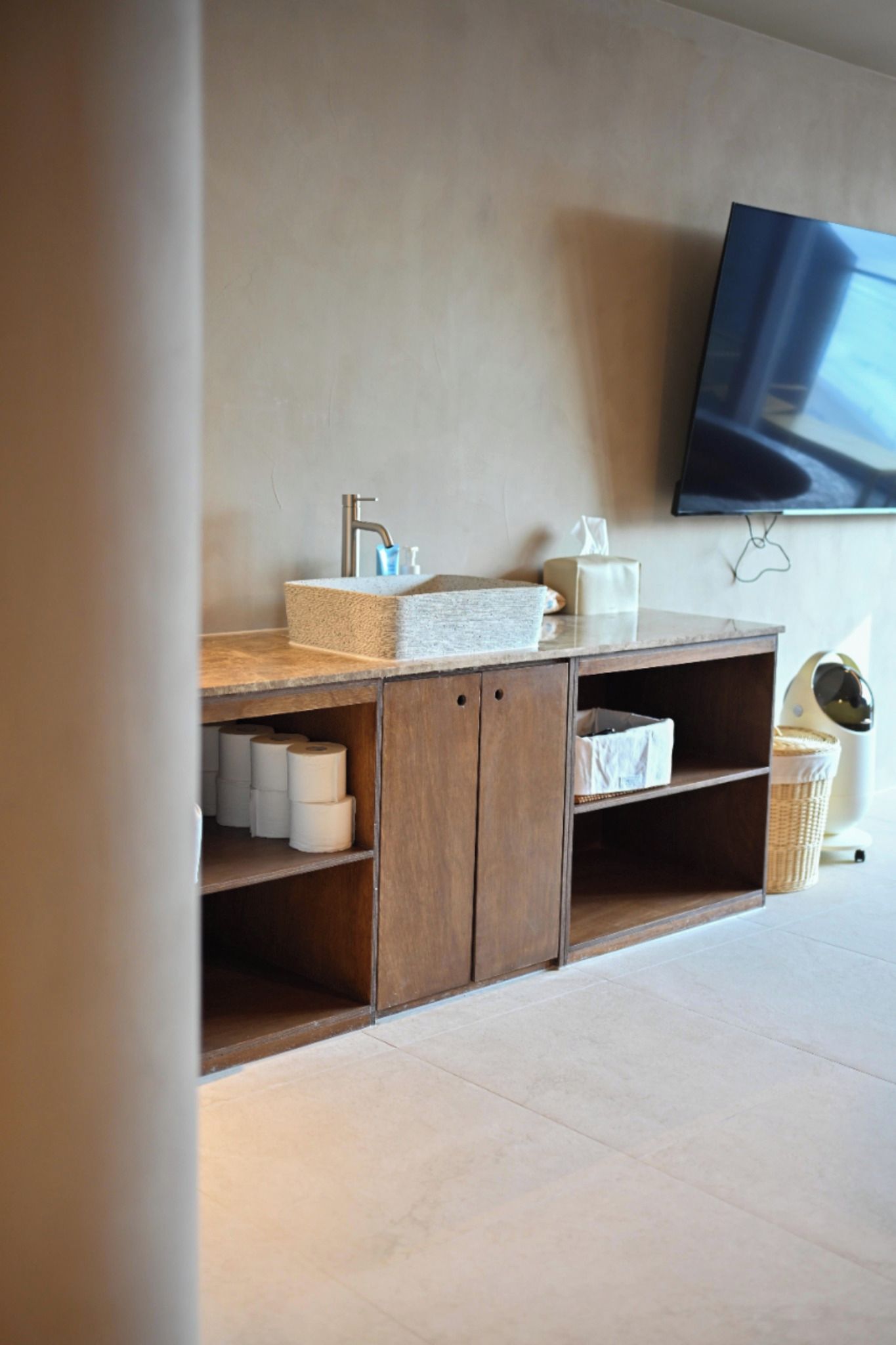 A bathroom with a wooden vanity, a mounted TV, and a wall-mounted toilet.