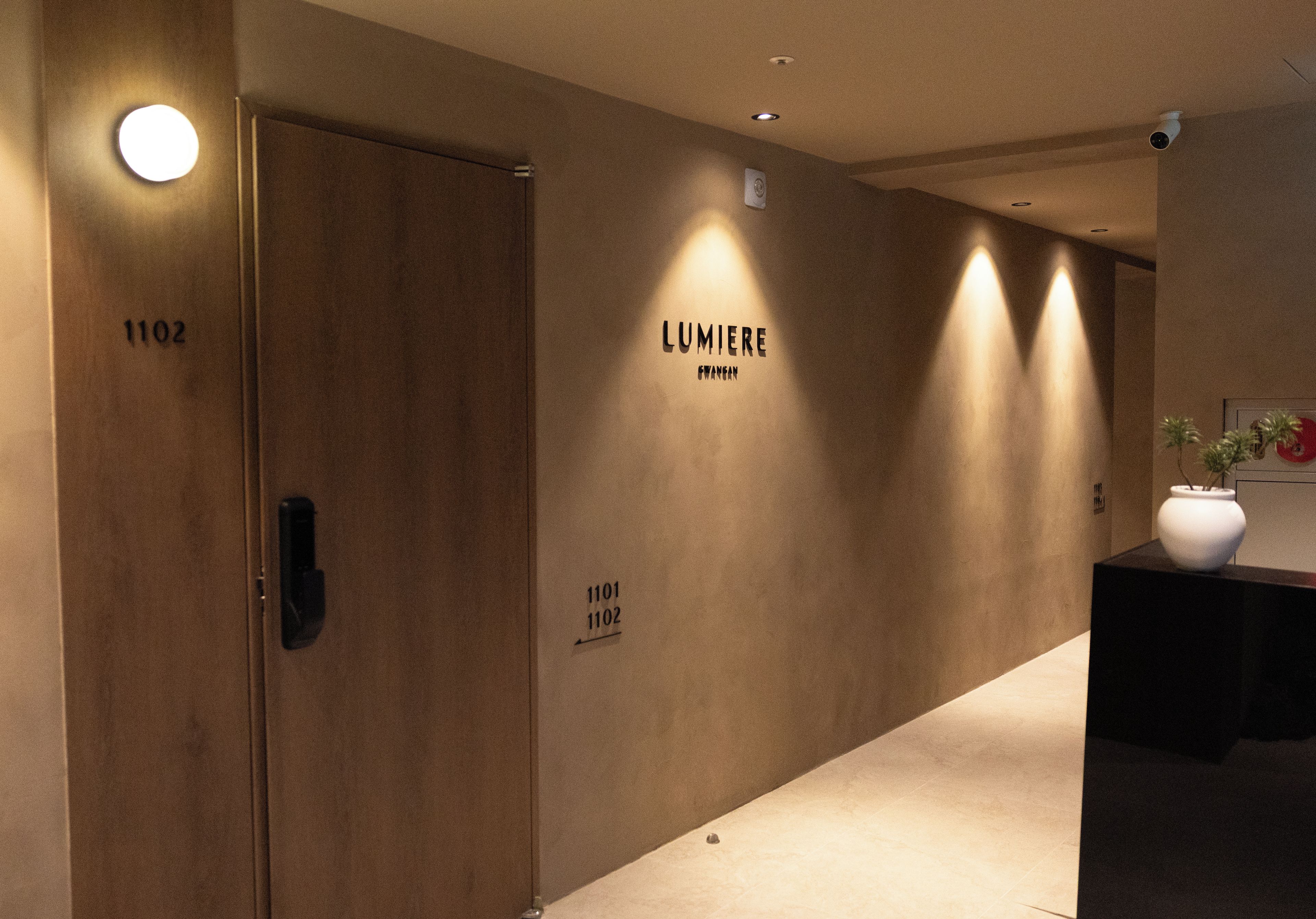A hallway with two doors labeled 1101 and 1102, a wall with the text 'LUMIERE GWANGAN', and a vase on a table.
