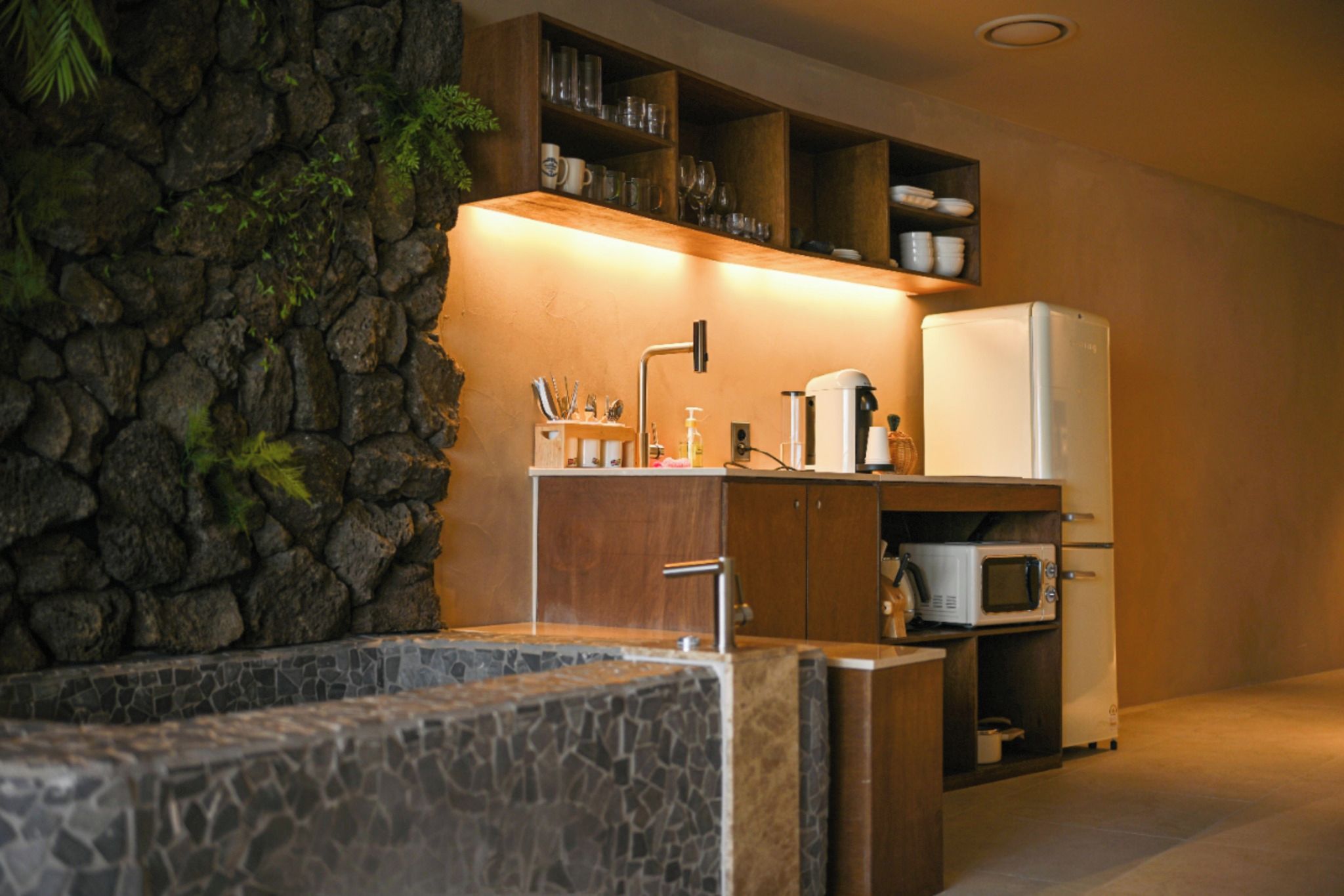 A kitchen with a stone wall, a sink, a microwave, and a refrigerator.