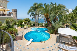 A pool area with a clear view of the sea, surrounded by palm trees and a stone tower. - AMORE RENTALS - Villa Imma with Swimming Pool and Sea View (Castellammare di Stabia)